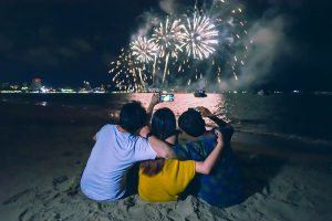Feux d'artifice en bord de plages avec trois enfants qui prennent des photos avec un téléphone portable